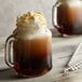 A glass mug filled with brown liquid and whipped cream next to a glass jar of brown liquid.