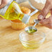 A hand pouring McCormick Culinary Imitation Lemon Extract from a bottle into a bowl of liquid.