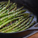 A skillet with asparagus cooking on a white background.