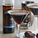 A glass of brown liquid next to a bottle of DaVinci Gourmet Sugar Free Chocolate Flavoring Syrup.