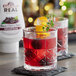 A glass of red liquid with orange slices and cherries on a table in a cocktail bar.