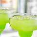 Two green margaritas with King Floyd's Sea Flake Rimming Salt on the rim on a table in a cocktail bar.