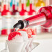 A person pouring Hawaiian Shaved Ice Watermelon syrup into a cup of snow cone ice.