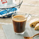 A glass cup of illy decaf coffee on a table with a pastry.