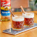 Two glasses of Torani butter rum flavoring syrup with brown liquid and cinnamon sticks.