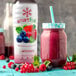 A close-up of a Smartfruit Blooming Berry Puree beverage bottle next to a glass of berries.