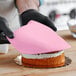 A person wearing black gloves and using a pink cloth to cover a cake with Satin Ice Baby Pink Vanilla Rolled Fondant.