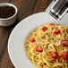 A bowl of spaghetti with tomatoes and black pepper next to a pepper mill.