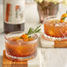 Two glasses of DaVinci Gourmet Old Fashioned drinks with rosemary sprigs on a wood and white surface.