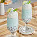 Two glasses of blue milkshakes with lime slices and whipped cream on top.