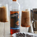 Two glasses of coffee with ice and DaVinci Gourmet Sugar Free Coffee Liqueur syrup next to a bottle of the syrup.