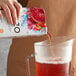 A hand pouring Tazo Sweetened Passion Iced Herbal Tea into a pitcher.