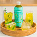 A basket with a bottle of Smartfruit Kiwi / Mint / Lemongrass juice and a glass of yellow liquid with a slice of kiwi and mint leaves.