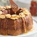 A bundt cake with almonds and honey drizzled on top.
