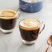 Two glass cups of Lavazza Espresso Maestro Ristretto on a table with a bowl of sugar and a copper spoon.