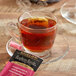 A glass cup of Bigelow Raspberry Royale tea with a tea bag on the side.