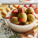 A bowl of Belosa Turkish red pepper stuffed green olives on a table with cheese and crackers.