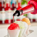 A person pouring Hawaiian Shaved Ice Bahama Mama syrup into a cup of ice.