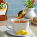 A hand holding a spoon pouring Dutch Gold Orange Blossom Honey into a cup of tea.