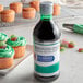 A bottle of McCormick green food color on a counter next to cupcakes.