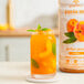 A bottle of Smartfruit Perfect Peach puree next to a glass of peach liquid.