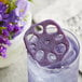 A glass of purple Lotus Root in Butterfly Pea and Elderflower Syrup with purple flowers on top.