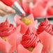 A close-up of a hand using a pastry brush to frost a cupcake with bright red frosting.