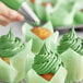 A hand using Chefmaster Leaf Green food coloring to frost a cupcake.