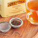 A strainer full of Twinings English Breakfast loose leaf tea next to a cup of tea.