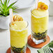 Two glasses of yellow Fanale banana smoothies with straws on a table.