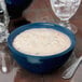 A Texas Blue melamine bowl of food on a table next to a glass of water and a plate.