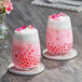 Two glasses of pink and white bubble tea with pink flowers.