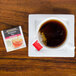 A glass cup of Bigelow Ceylon tea on a saucer with a packet of tea on the side.