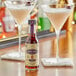A glass of lavender colored liquid next to a bottle of Scrappy's Lavender Bitters.
