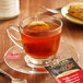 A glass cup of Bigelow spiced chai tea with a tea bag on a saucer on a table with cookies.