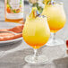 Two glasses of yellow liquid with fruit on top on a table.