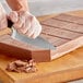 A person's hand using a knife to cut a Callebaut milk chocolate block.