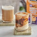 A glass mug of Oregon Chai Salted Caramel Chai Tea Latte with a box of Oregon Chai Latte Concentrate on a table.