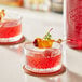 A red cocktail with a cherry and a stick on top.