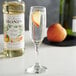 A glass of champagne with a Monin white peach flavoring syrup on a table.