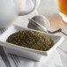 A bowl of Regal Crushed Spearmint leaves next to a tea strainer and a teapot.