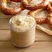 A pretzel with mustard next to a jar of Regal Yellow Mustard Seed.