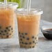 A plastic cup of brown bubble tea with black balls and a lid.