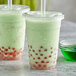 Two plastic cups of green bubble tea with straws.