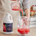 A person pouring Capora Raspberry fruit smoothie mix into a blender.