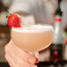 A hand holding a glass of pink liquid with a strawberry on top.