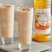 Two glasses of pumpkin pie milkshake with Monin pumpkin pie syrup and a bottle of Monin pumpkin pie syrup.