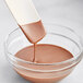 A spoon pouring Cacao Barry blonde compound coating into a bowl of liquid.