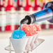 A person pouring Hawaiian Shaved Ice Blue Raspberry syrup over a blue and red snow cone.