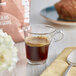 A glass cup of Lavazza coffee on a table next to a spoon.